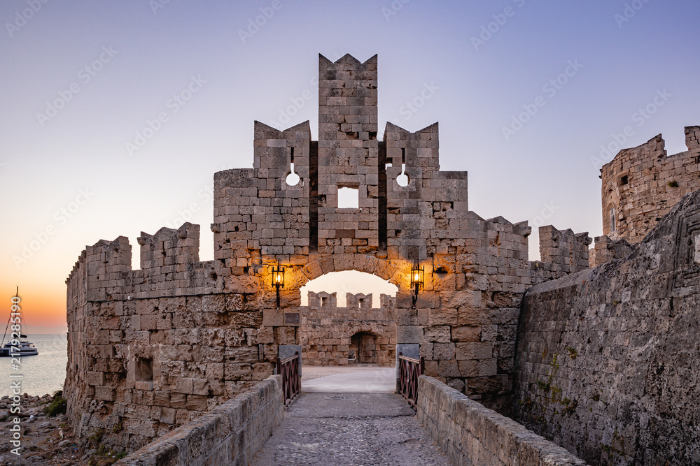 Obraz premium Saint Paul's Gate (Pyli Agiou Pavlou) at Dusk, Medieval Old Town of Rhodes, Greece — Stone fortification walls and arched entrance illuminated by lanterns