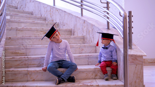 Fotografie Children sitting on stair and playing with graduation caps