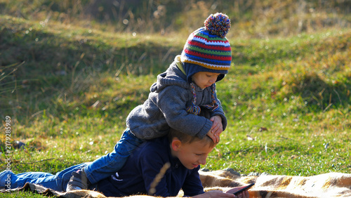 Принти на полотні Cute little child riding big brother watching mobile phone in nature