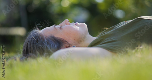Картината върху платно Mid-age woman laid back on green lawn and dreaming with closed eyes, day dreamer