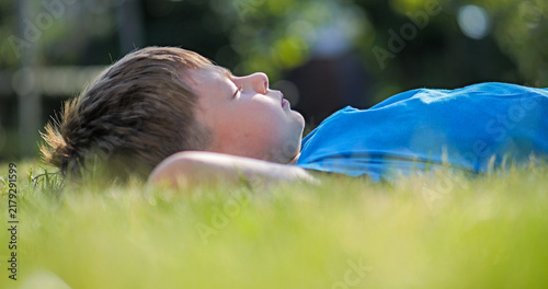 Little kid laid back on lawn grass, daydreaming with closed eyes outdoor in nature
