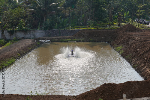 Obraz na płótnie Floating paddle wheel aerator operating in earth fish pond splash water to oxygenate aquaculture reservoir, freshwater fish farming, shrimp aquaculture, and water aeration technology concept