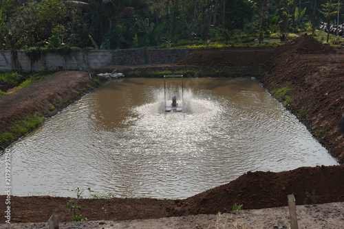 Floating paddle wheel aerator operating in earth fish pond splash water to oxygenate aquaculture reservoir, freshwater fish farming, shrimp aquaculture, and water aeration technology concept.