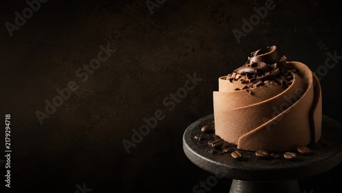 Elegant individual chocolate mousse cake with chocolate curls and coffee beans on a dark stand with moody background