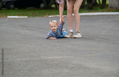 Little boy lying on asphalt ground during tantrum while mother pulling his arm trying to lift him up.