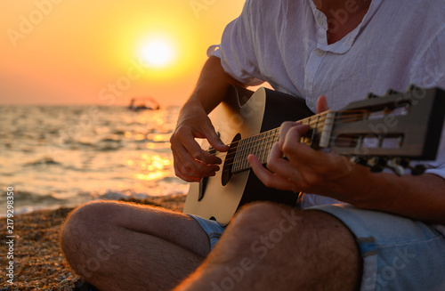 A musician on the seashore. The guitarist plays against the backdrop of a sunset. Close-up, selective focus.