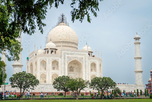 Beautiful side view of the iconic white marble mausoleum dome and minaret surrounded by green trees and garden lawn at the Taj Mahal complex in Agra, Uttar Pradesh, India.