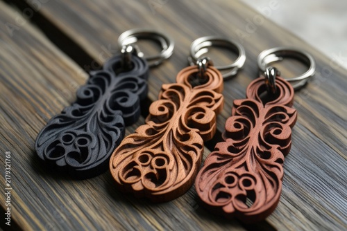 Decorative wooden keychains with intricate carvings in black, brown, and orange hues, displayed on a rustic wooden surface, showcasing craftsmanship and artistic design elements