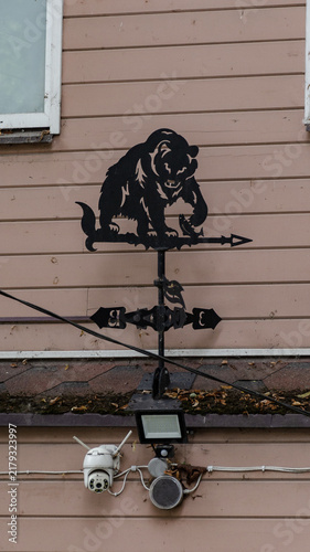 Black metal weather vane with bear silhouette on wooden wall