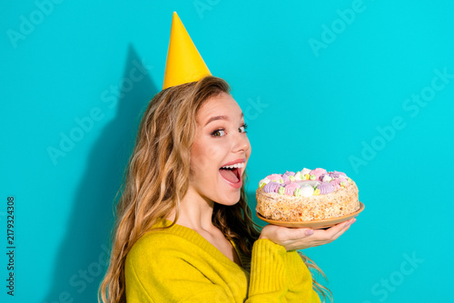 Photography Young woman with blonde hair wearing a yellow party hat holds a colorful cake ag