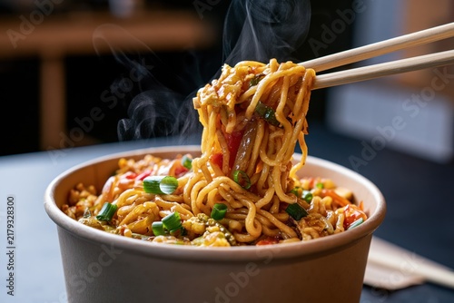 Chopsticks lifting steaming stir-fried Asian noodles with vegetables