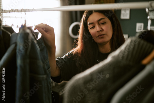 Quadro su tela Young biracial woman browsing clothes on rack in studio
