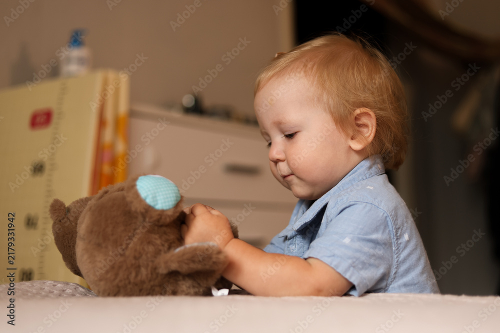 Naklejka premium Toddler boy playing with a stuffed animal on a bed