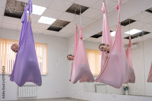 Fotografie Gravity defying stretching practiced by women using colorful silk hammocks insid