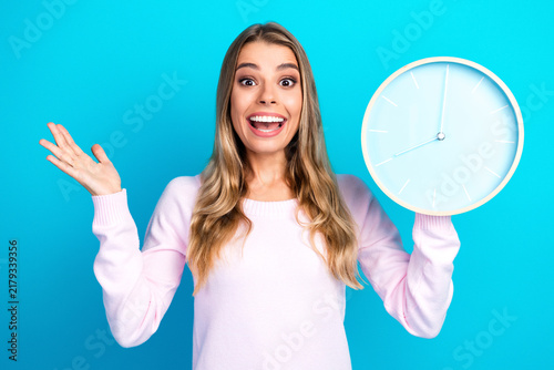Foto Happy young woman holding wall clock and smiling, expressing excitement about ti