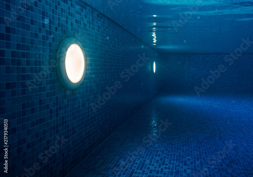 Underwater view of an empty luxury swimming pool with dark blue mosaic tiles and glowing warm wall lights