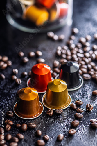 Colorful Coffee Capsules and Espresso Pods Scattered Among Roast Coffee Beans on Dark Surface