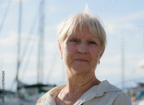 Portrait of a mature woman standing near marina in sunlight.