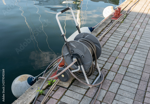 Dockside hose reel by calm marina water, industrial utility equipment