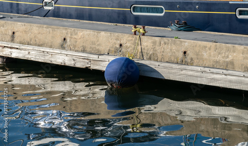Blue mooring buoy beside docked boat and reflective harbor water.