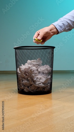 Картината върху платно Hand dropping a used battery cell into a black mesh trash bin filled with crumpl