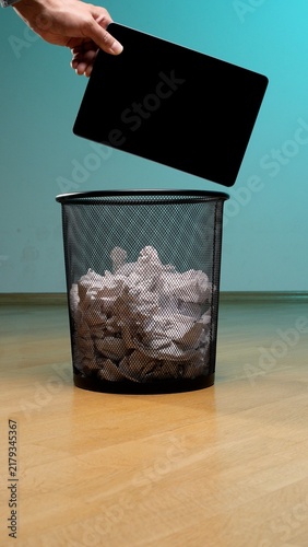 Foto Hand placing a tablet into a full mesh trash bin, symbolizing digital detox, dat