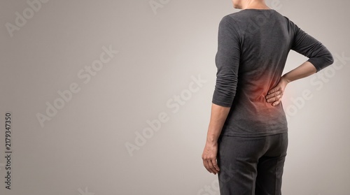 Woman suffering from lower back pain holding her lumbar spine with highlighted injury area
