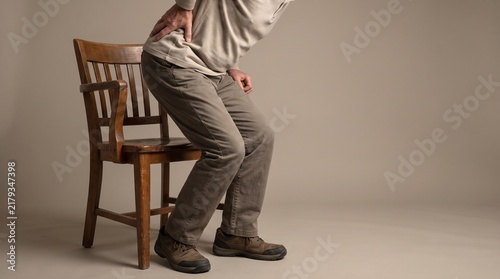Man standing up from a wooden chair suffering from severe lower back pain and lumbar ache.