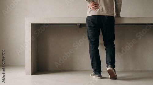 Professional woman holding back pain standing in minimalist office space with neutral lighting