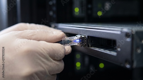 Obraz na płótnie Technician plugging a glowing ethernet cable into a server port.