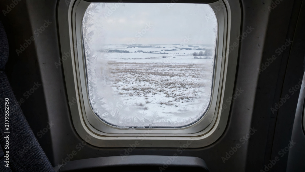 Obraz premium Frosted airplane window over snowy landscape