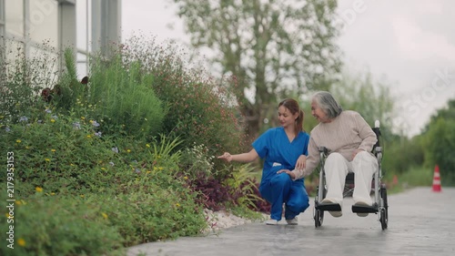 Caregiver walking with senior in wheelchair outdoors