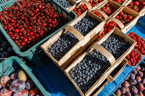 Fresh organic Vaccinium corymbosum blueberries, Prunus avium sweet cherries, Fragaria strawberries, Rubus idaeus, and Prunus domestica plums displayed on an outdoor farmers market in Warsaw, Poland.
