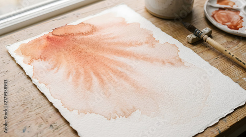 Watercolor Artist Workspace with Terracotta Paint Bloom on Wooden Desk
