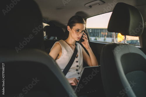 Businesswoman talking on a smartphone while using a laptop in the back seat