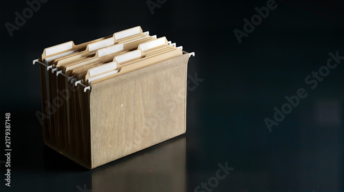 Naklejka Professional hanging file folder box with manila folders and blank white labels on a dark reflective surface for office document management.