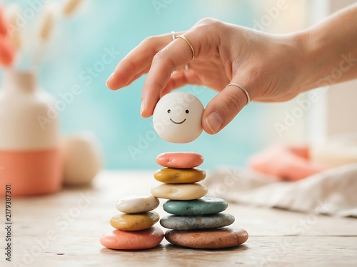 A person placing a small smiling sphere on top of a stack of colorful smooth stones.