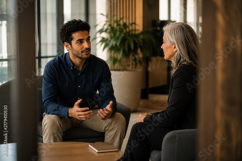 Young man and senior woman having a focused conversation in a modern office, suggesting mentorship, consultation, collaboration, and professional guidance.