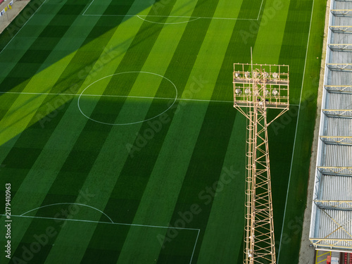 Aerial view of a football pitch with a tall floodlight tower and striped grass patterns in the United Kingdom.