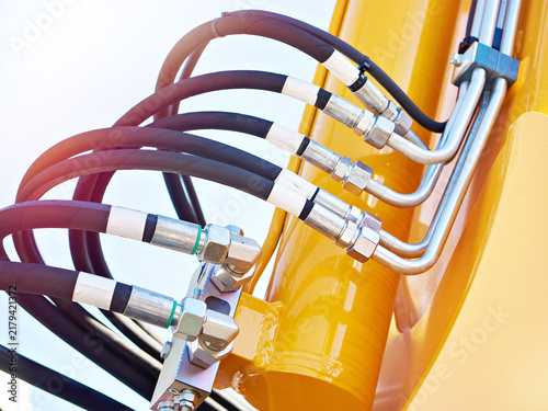 Hydraulic hose connections on yellow excavator cylinder