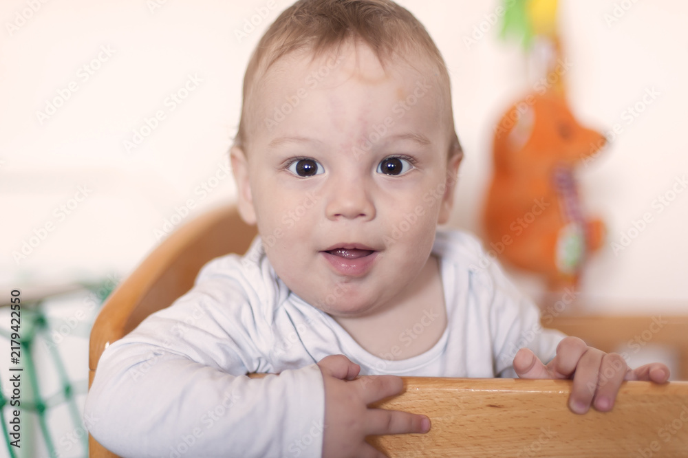 Fototapeta premium Cheerful toddler boy smiling from his wooden crib in a bright nursery