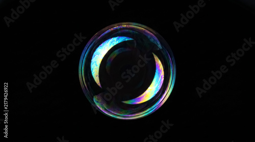 a single iridescent soap bubble with crescent pattern floats against a black background