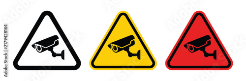 Surveillance Warning Signs: A trio of cautionary signs—black, yellow, and red—each featuring a silhouette of a surveillance camera, warn of monitoring and security presence.