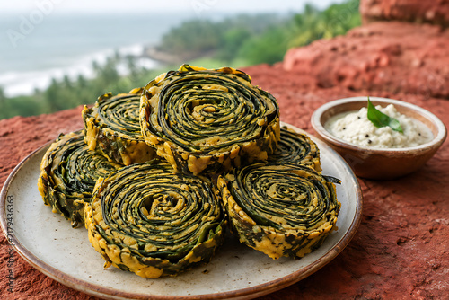Konkan-style colocasia leaf alu vadi, intricate dark-green spirals with golden spiced gram-flour layers, stacked irregularly beside a tiny coconut chutney bowl, red laterite stone backdrop
