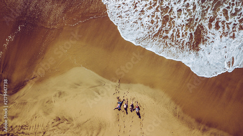 Photography Friends relaxing on warm sand by the ocean seen from above, waves lapping the sh