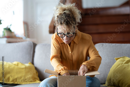 Fotografie Woman excitedly opening a cardboard package delivered to her home, experiencing