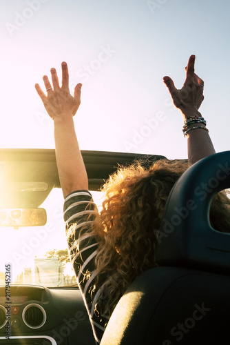 Foto Woman with curly hair standing in a convertible with arms raised, basking in gol