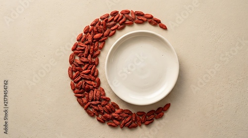 A high angle goji berries top view arranged in a crescent moon shape around a white ceramic bowl on table