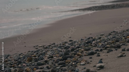 Low-angle view of many small stones on a beige sandy beach with gentle waves quietly washing ashore in the background