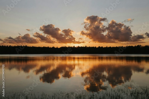 Golden sunset reflection over calm lake water with scenic cloudscape and forest silhouette at dusk